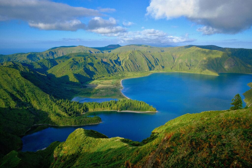 Explore the serene beauty of a lush green landscape with a tranquil lake on São Miguel Island.