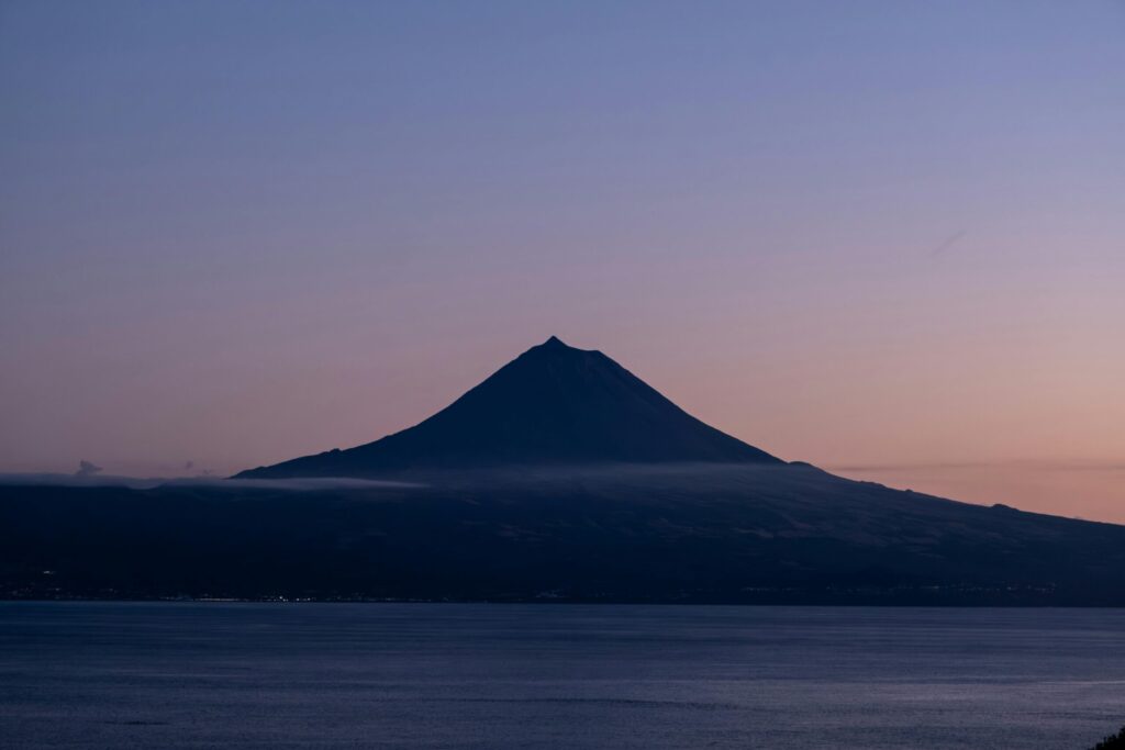 Silhouette of a volcano at dusk with a serene ocean in the foreground, capturing tranquility.